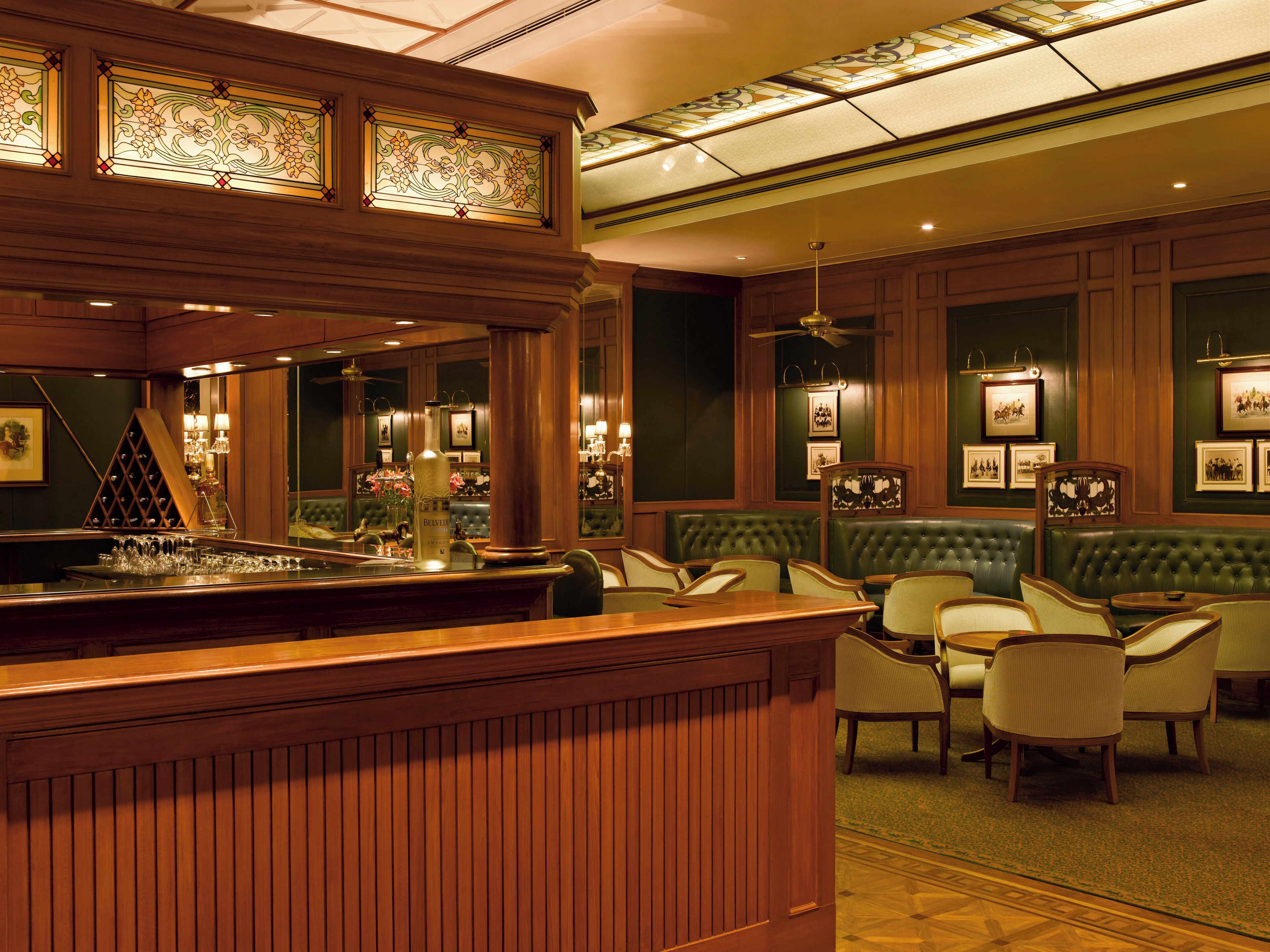 A bar area with a wooden counter, green upholstered seating, and framed pictures on the walls.