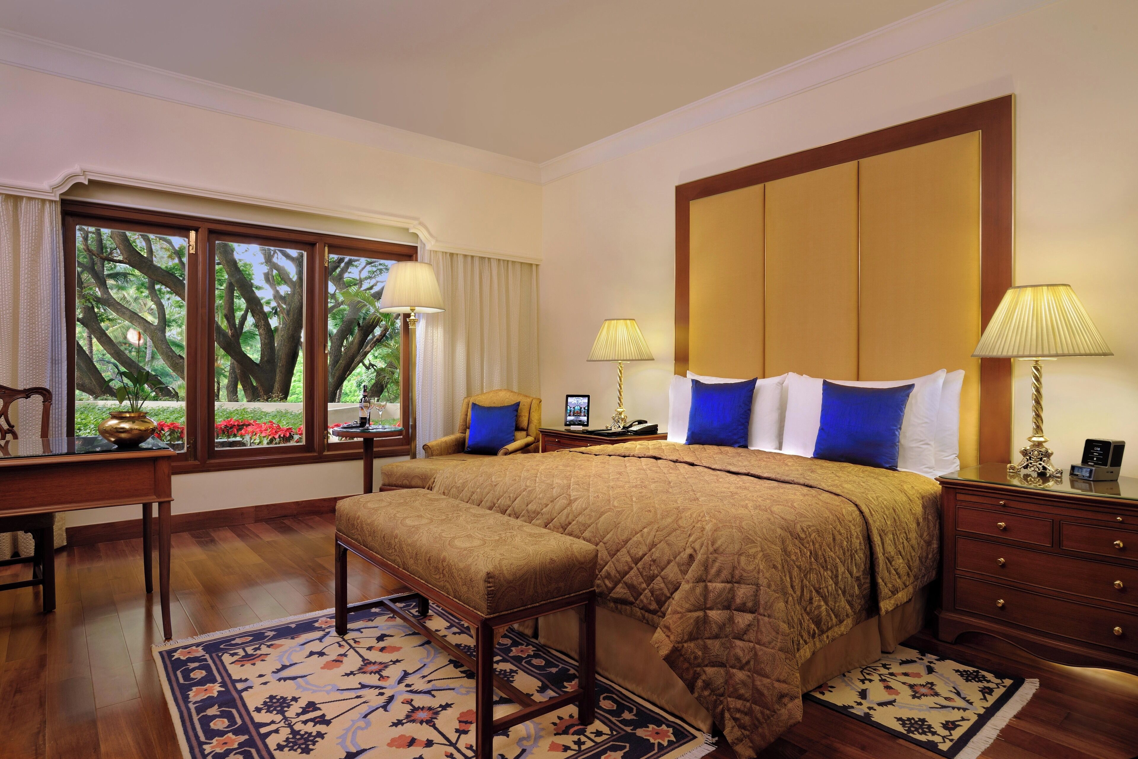 Habitación de hotel con una cama grande, un banco, un escritorio y vistas a árboles a través de la ventana.