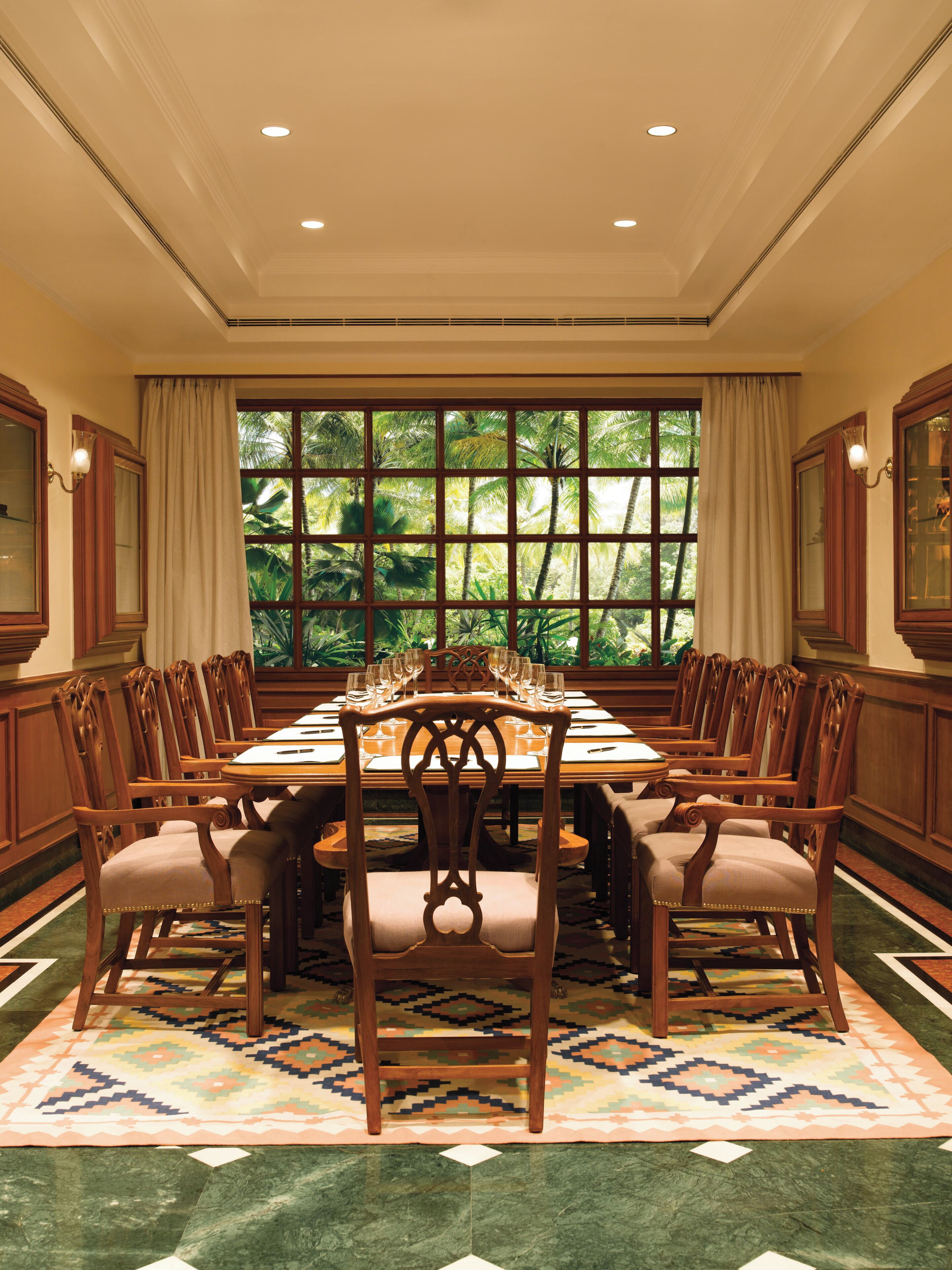 Une salle à manger élégante, avec une grande table, des chaises en bois et une vue sur les palmiers par la fenêtre.