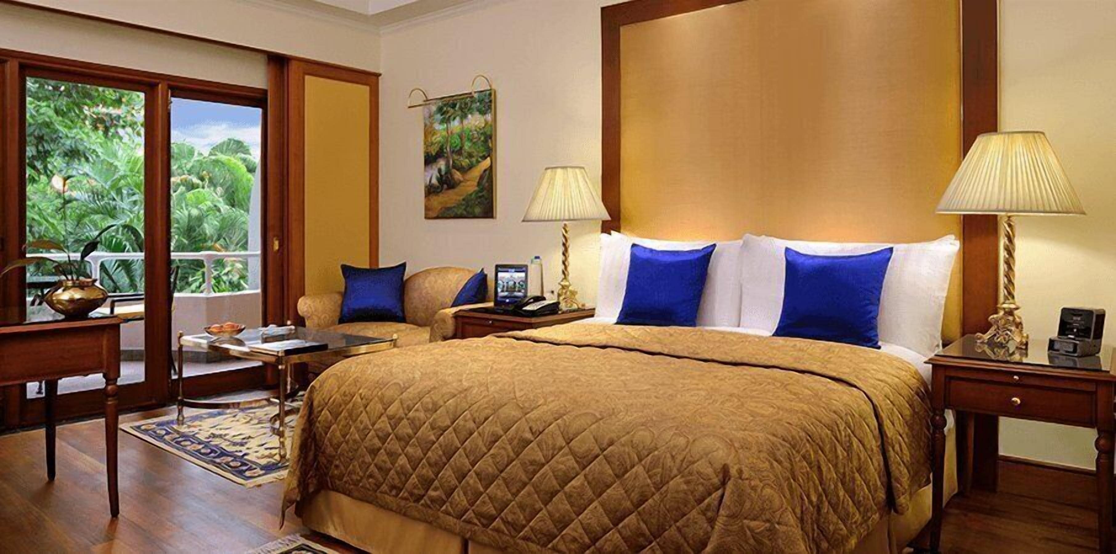 Une chambre d’hôtel avec un grand lit, deux tables de chevet, un bureau et une chaise. Il y a une fenêtre donnant sur un paysage verdoyant.
