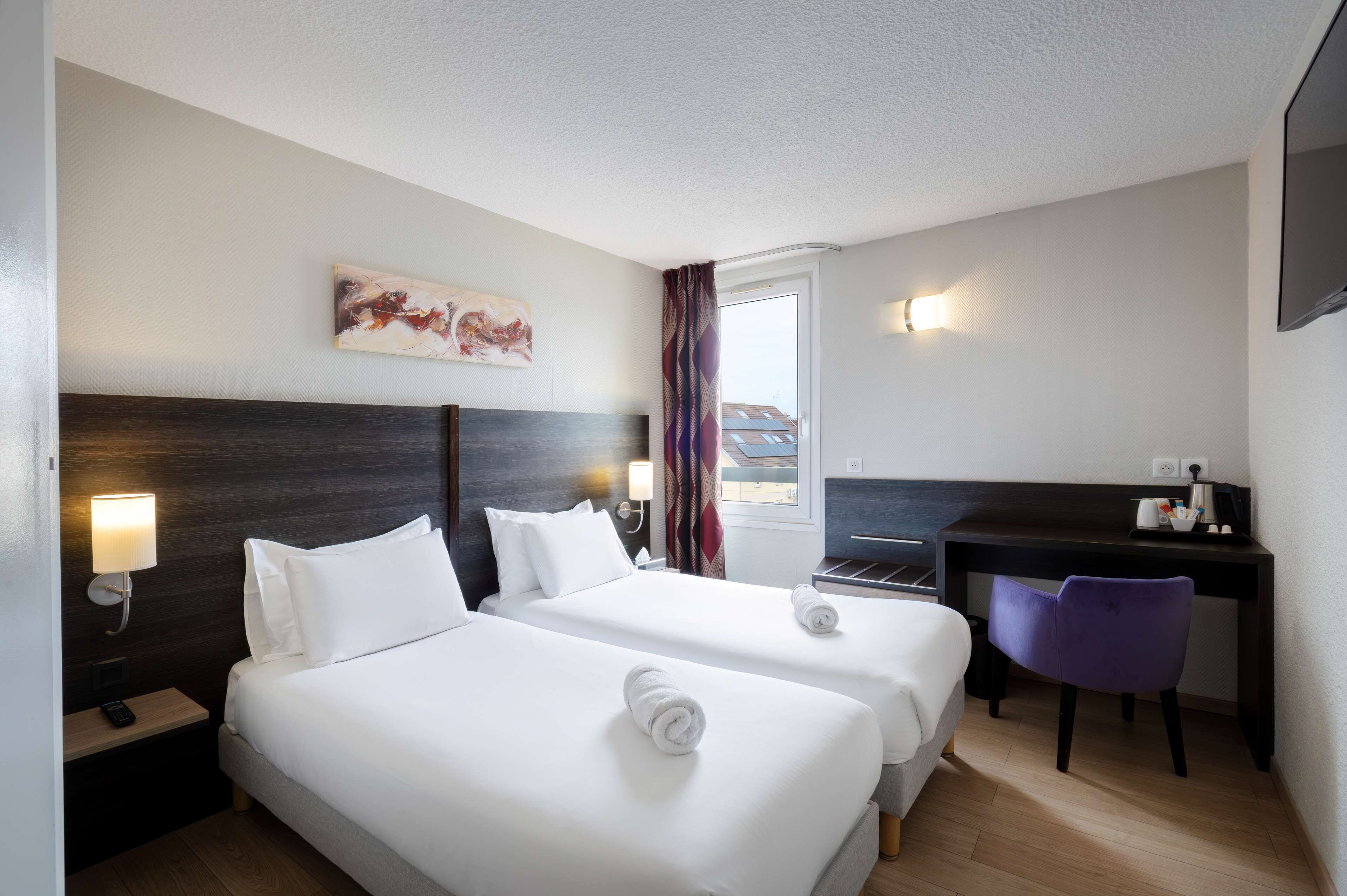 Habitación de hotel con dos camas, un escritorio, una silla, un cuadro y una ventana con cortinas.