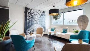 A modern lounge area with a white sofa, teal chairs, and a large black and white mural. - Kyriad Belfort Centre Gare (Belfort)