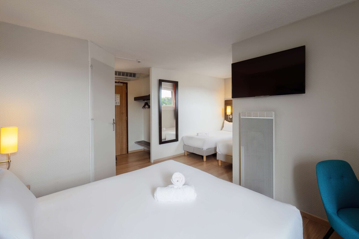 Habitación de hotel con cama, televisor montado en la pared, una silla y un baño visible a través de una puerta abierta.