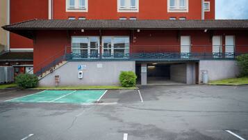 Un edificio con facciata rossa, ingresso coperto e area parcheggio con posti delimitati.