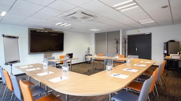 Ein Konferenzraum mit großem Tisch, Stühlen, einer Tafel und einer Projektionsleinwand.