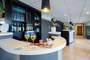 Un área de bar moderna con una barra curva, copas de vino, botellas y diversos aperitivos.