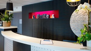A reception desk with a 'Smile' sign, a potted plant, and a wall-mounted light fixture. - Kyriad Belfort Centre Gare (Belfort)