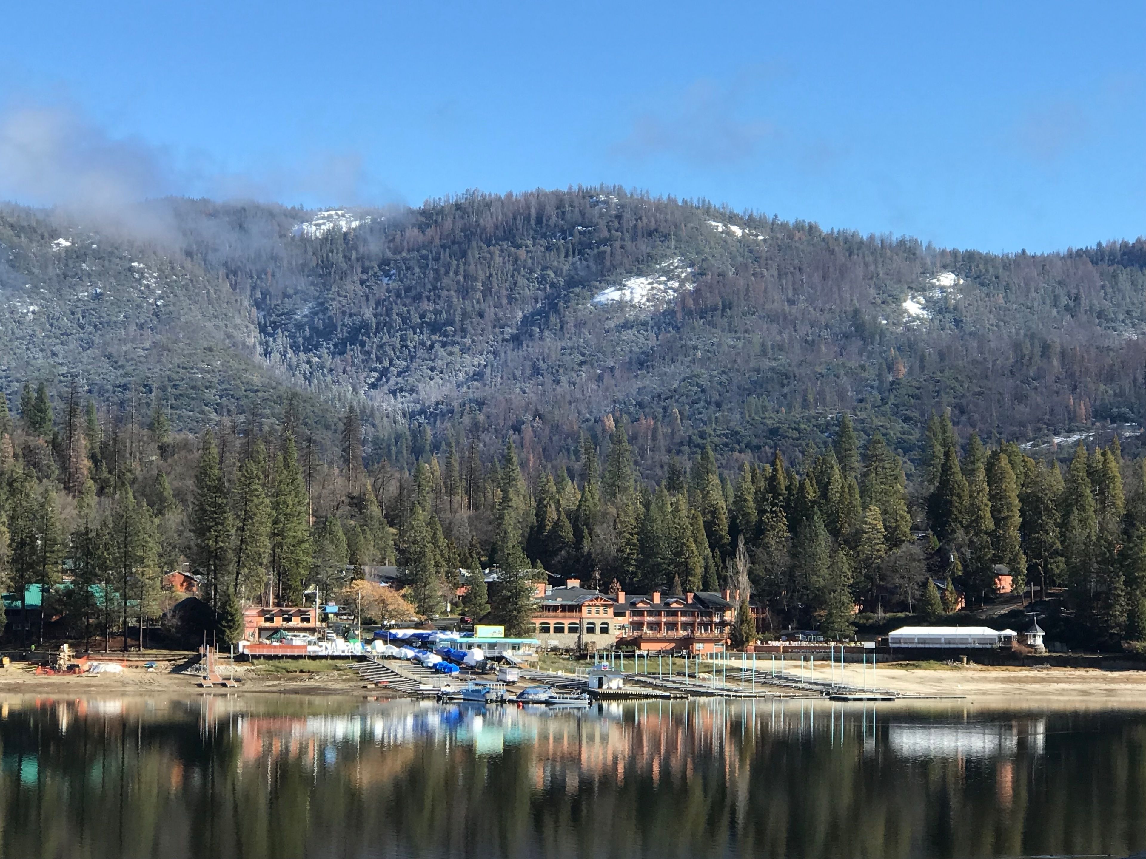 Une vue sur un lac, avec un quai, des bâtiments et une montagne boisée en arrière-plan.