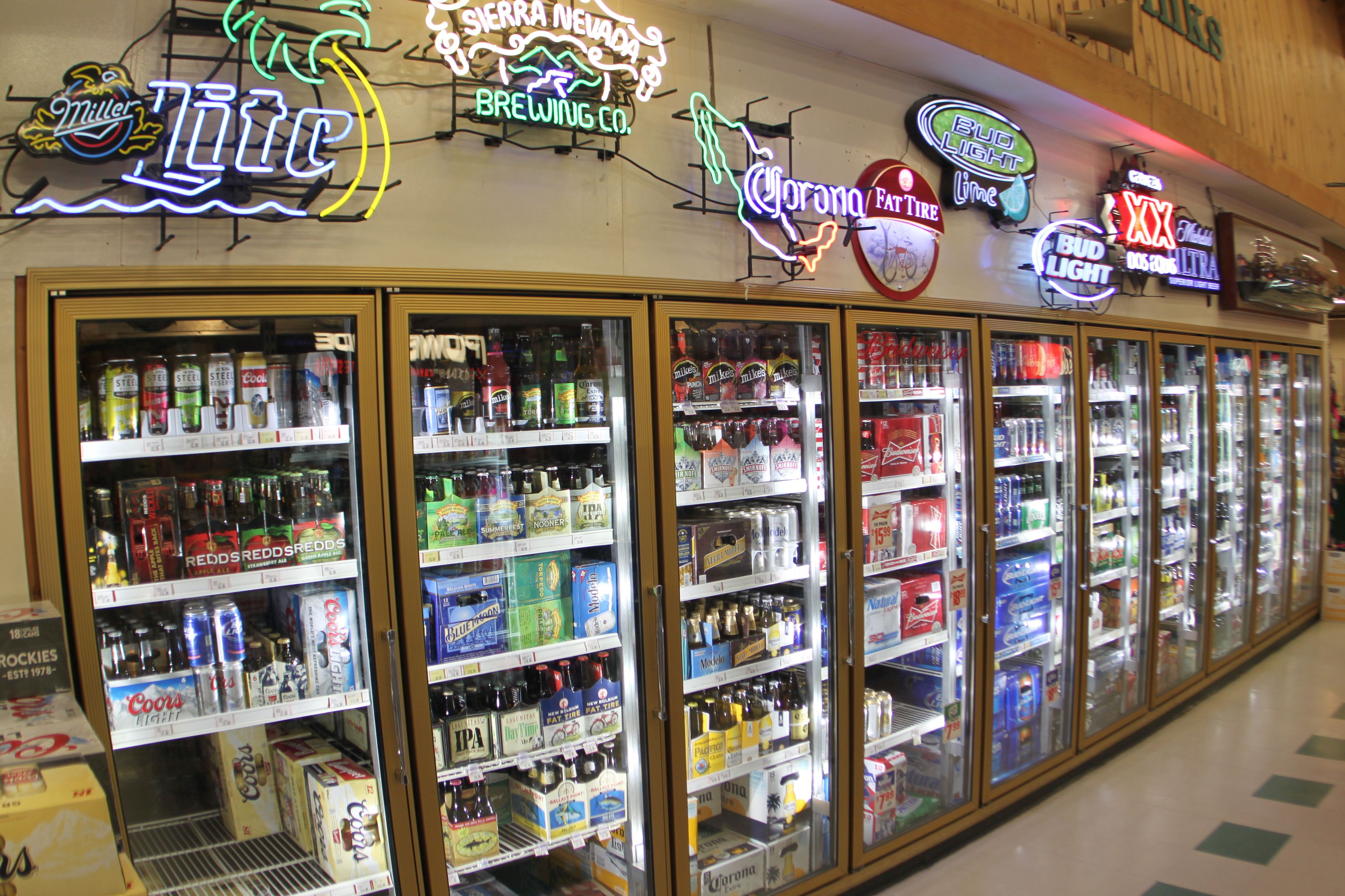A row of refrigerated beverage display cases in a store, with various brands of beer and soda visible.