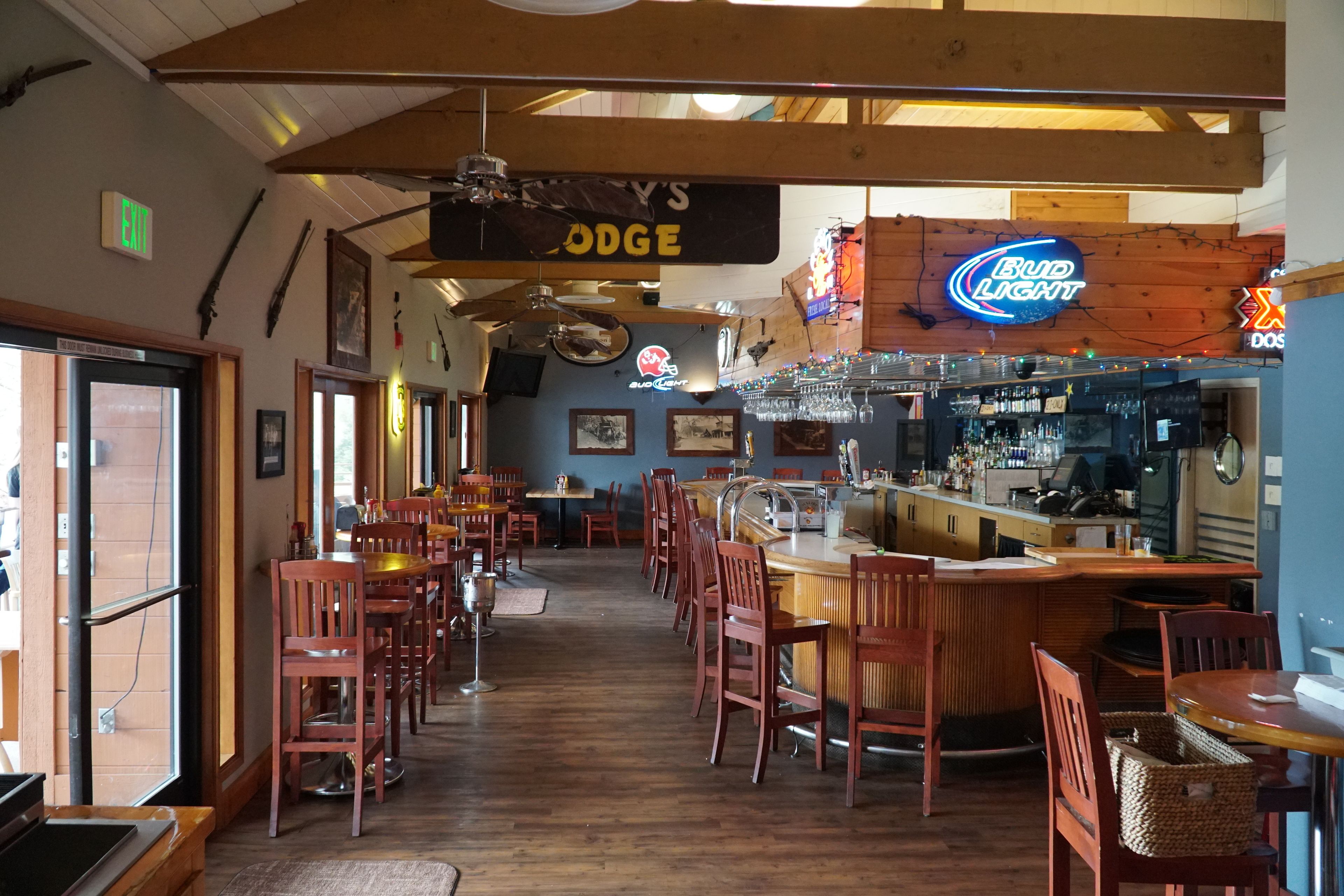 A cozy restaurant interior with wooden floors, a bar area, and a 'Bud Light' neon sign.