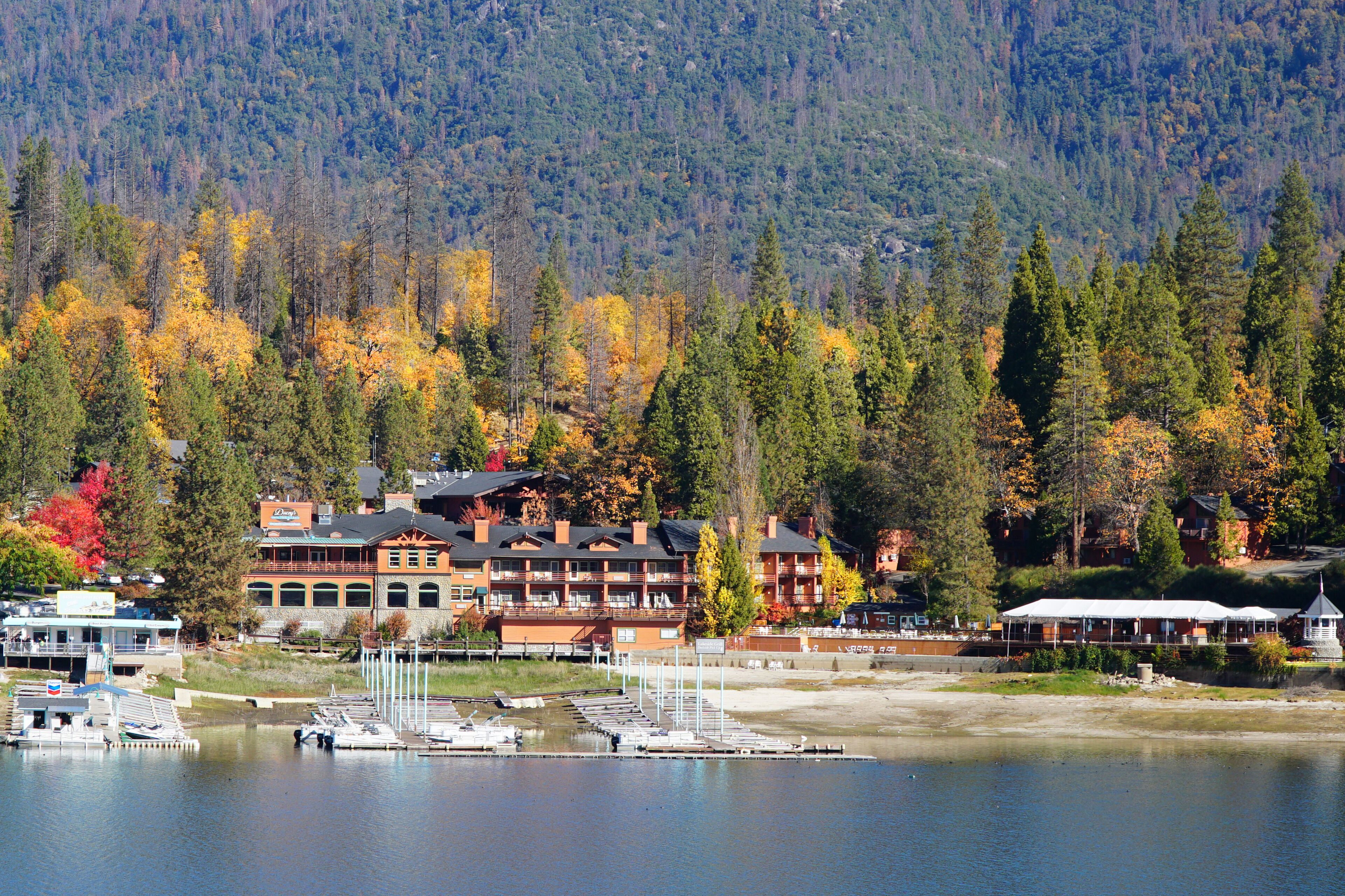 Un chalet au bord du lac, composé de plusieurs bâtiments, avec des bateaux amarrés et une montagne boisée en arrière-plan.