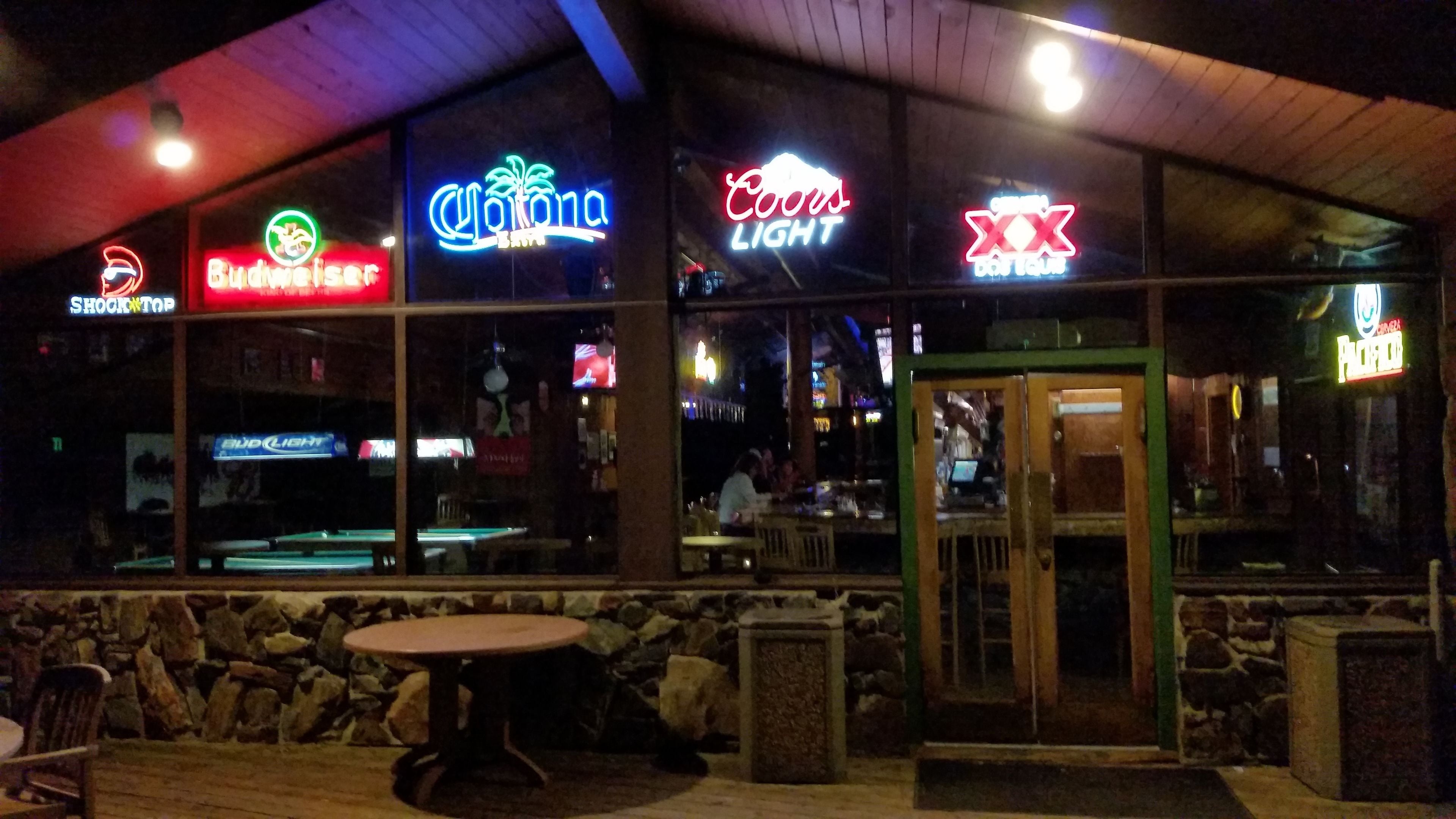 A bar with neon signs for Budweiser, Corona, Coors Light, and XXX.