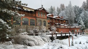 A large, multi-story building with a stone facade and green-framed windows, surrounded by snow-covered trees.