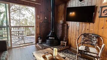 A cozy cabin interior with a wooden interior, a fireplace, a television, and a large window overlooking a deck.