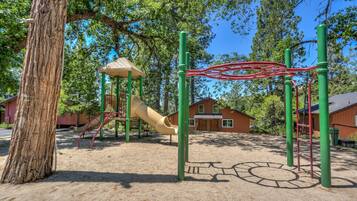 Children can play on the slide and climbing structures in this playground surrounded by trees and a building.