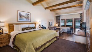A spacious bedroom with a large bed, a desk, and a view of the outdoors through the windows.