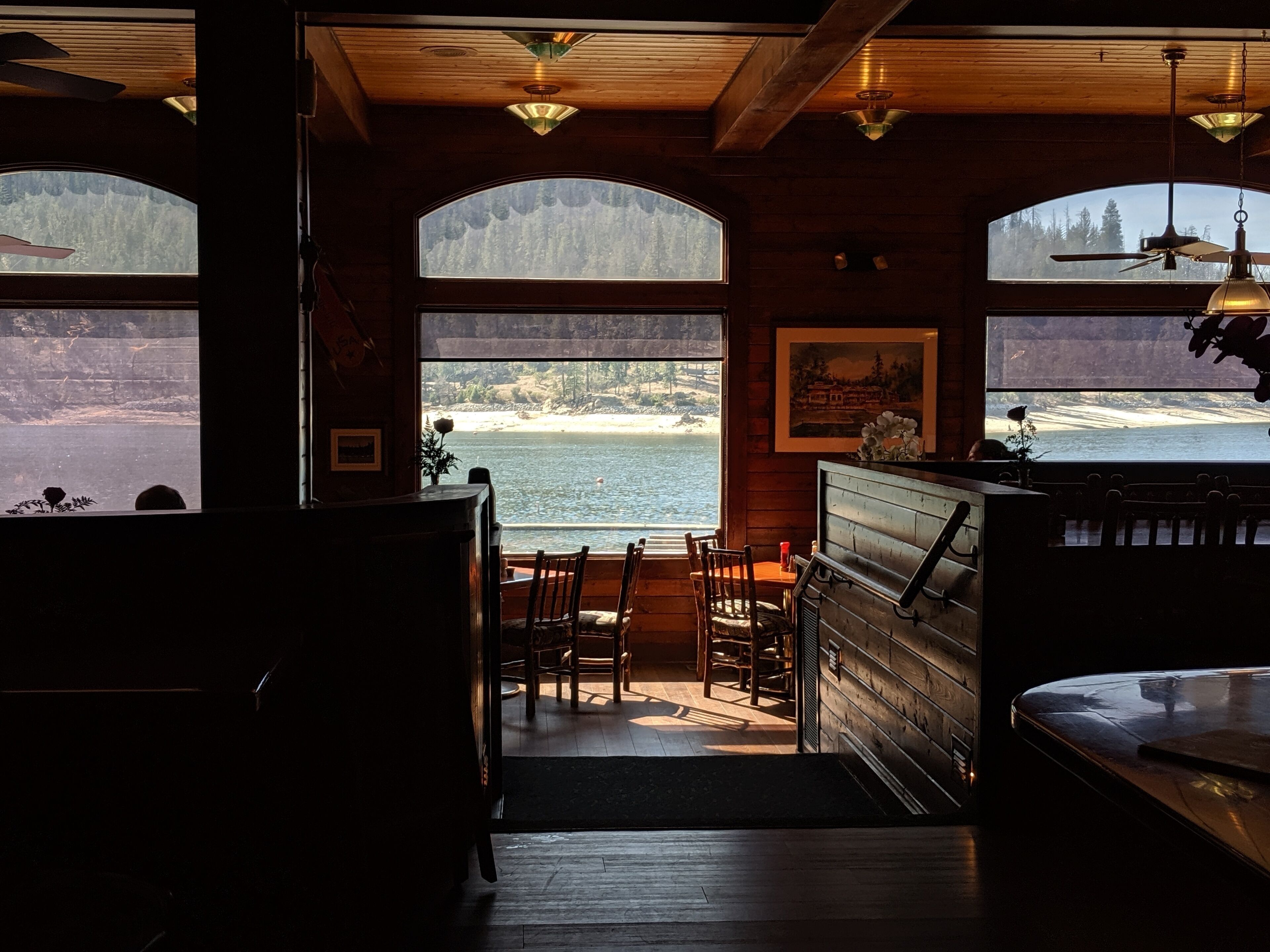 A cozy interior with wooden walls, a bar area, and large windows overlooking a beach.
