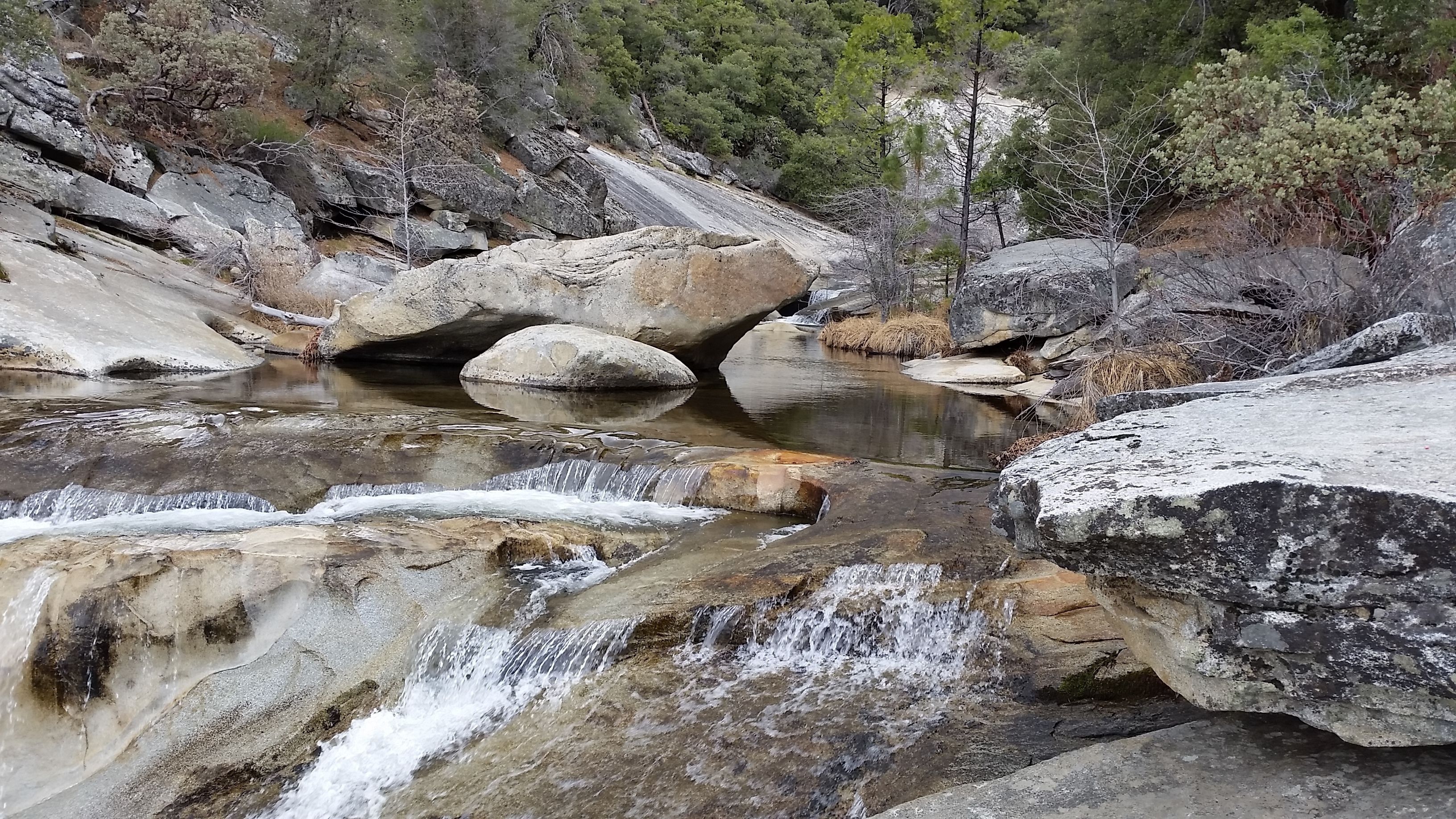 Eine natürliche Landschaft mit einem kleinen Wasserfall, felsigem Gelände und spärlicher Vegetation.