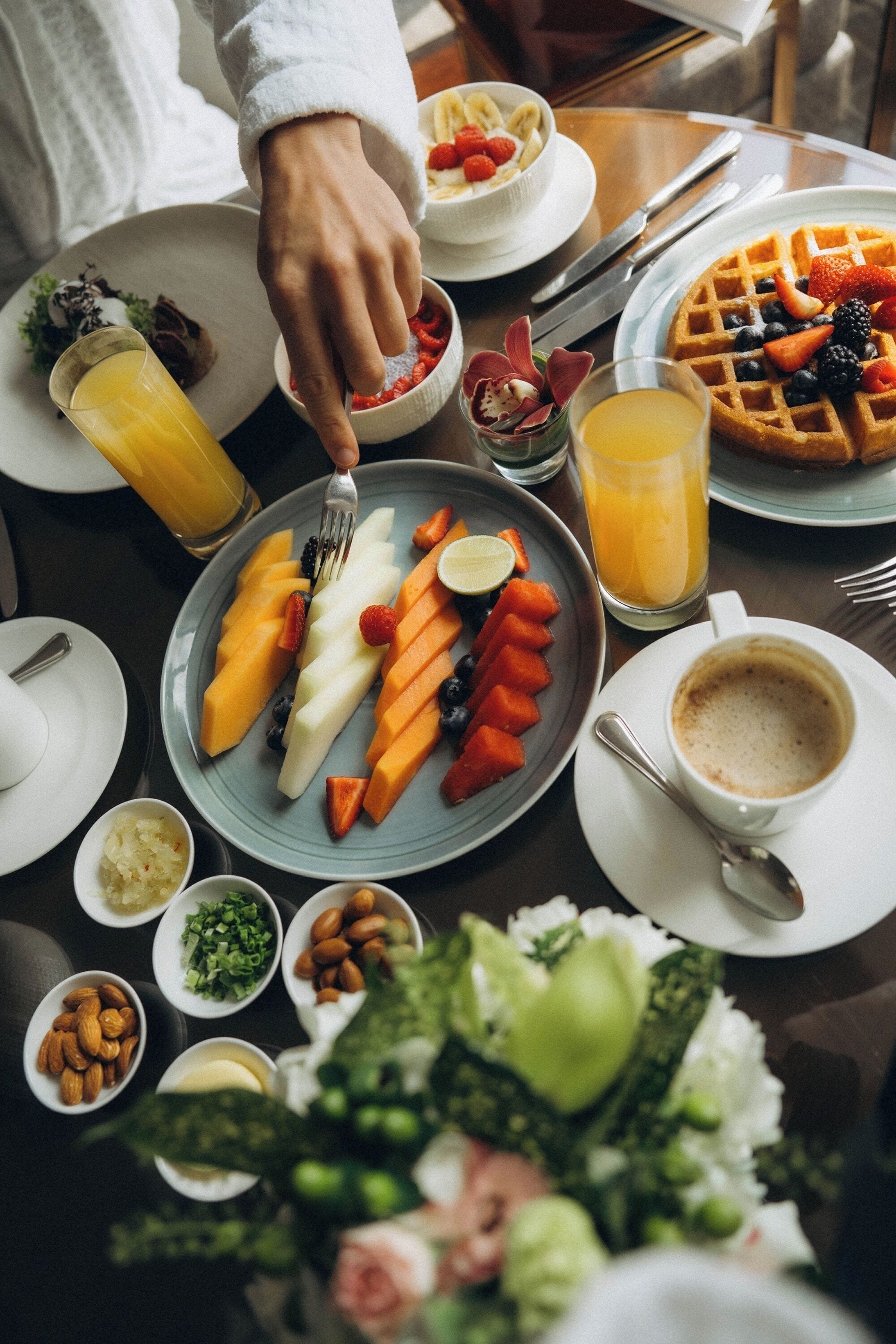 A breakfast setting with plates of fruit, waffles, and coffee.