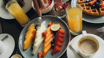 A breakfast setting with plates of fruit, waffles, and coffee.
