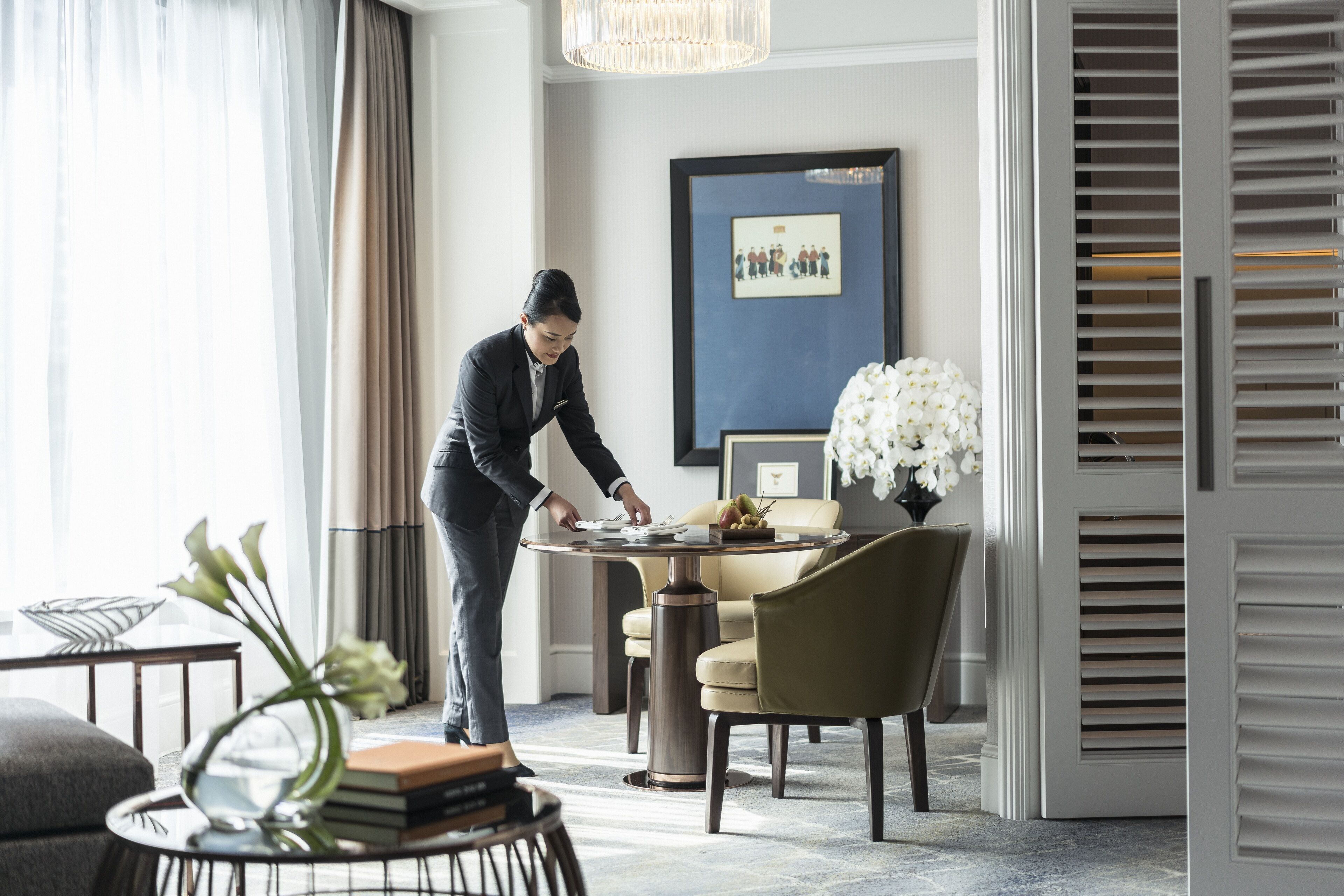 A modern hotel room with a dining area, a framed picture on the wall, and a vase of flowers on the table.