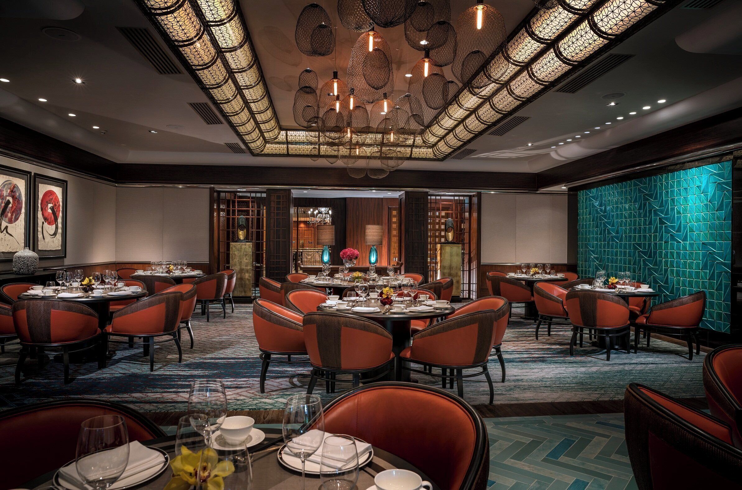 A spacious dining area with round tables and red chairs, a patterned carpet, and a decorative ceiling.