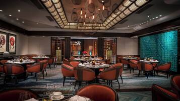 A spacious dining area with round tables and red chairs, a patterned carpet, and a decorative ceiling.