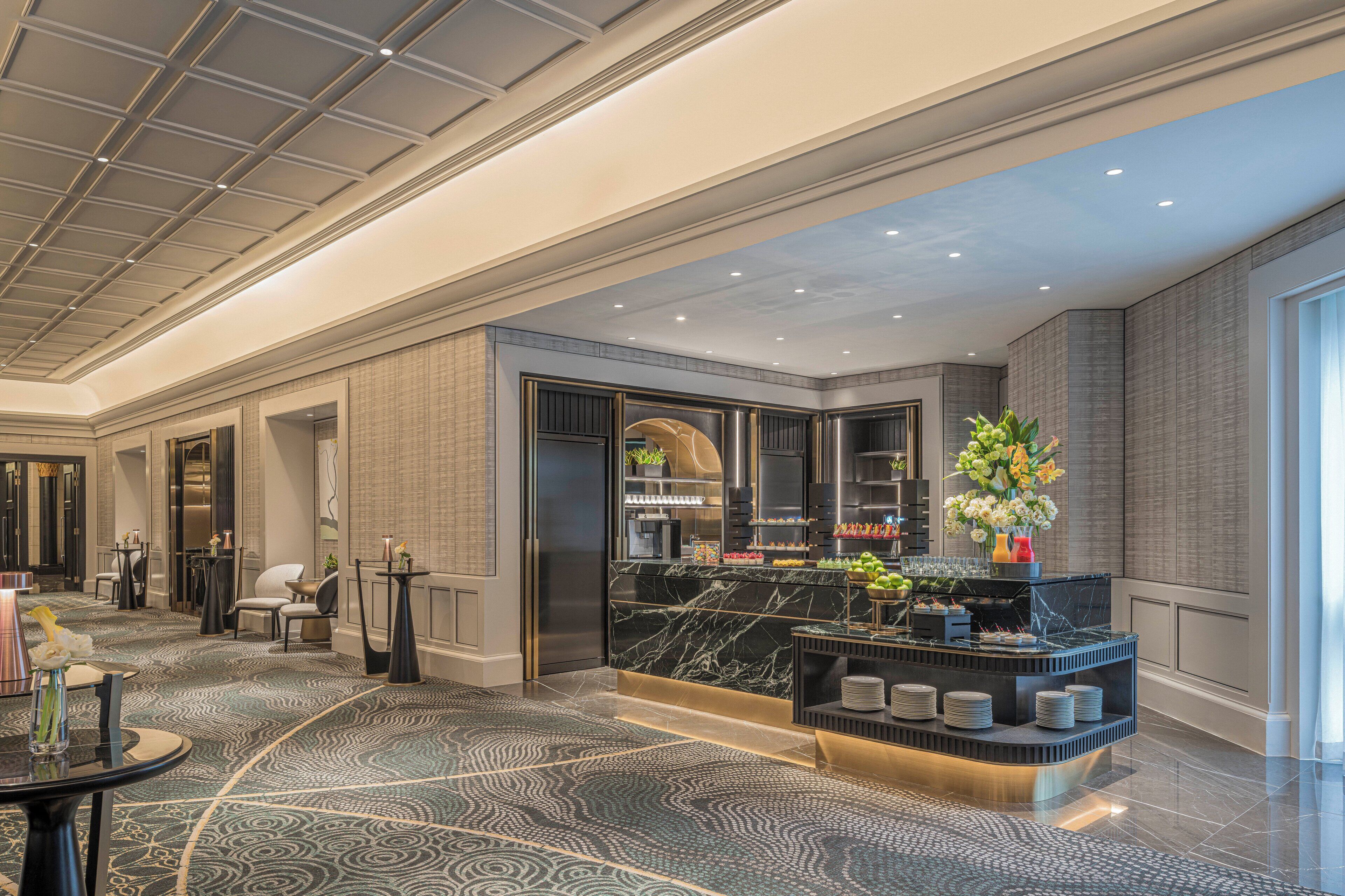 A modern hotel lobby with a marble reception desk, seating area, and a large window providing natural light.