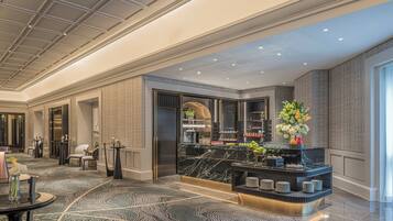 A modern hotel lobby with a marble reception desk, seating area, and a large window providing natural light.