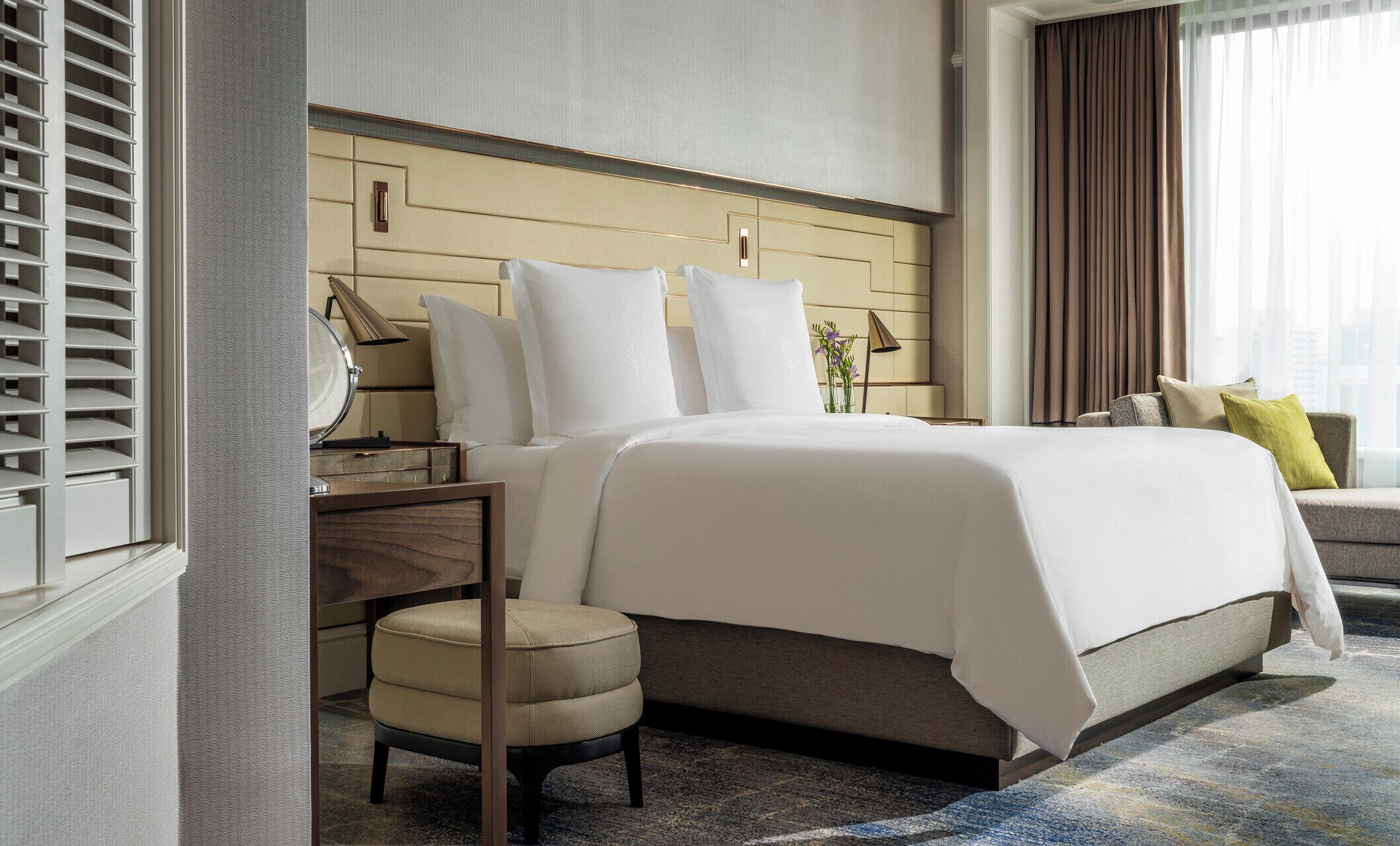 Et hotelværelse med seng, natbord, lampe, stol og udsigt over byen fra vinduet.