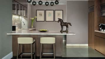 A modern kitchen with a marble countertop, two bar stools, a decorative horse sculpture, and framed botanical prints on the wall.