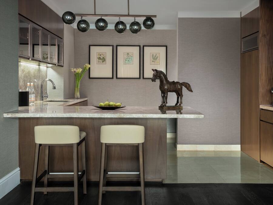 A modern kitchen with a marble countertop, two bar stools, a decorative horse sculpture, and framed botanical prints on the wall.