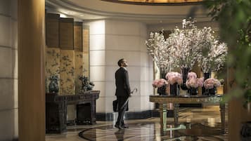 Un hombre con traje camina por un vestíbulo con un arreglo floral grande y un piso pulido.