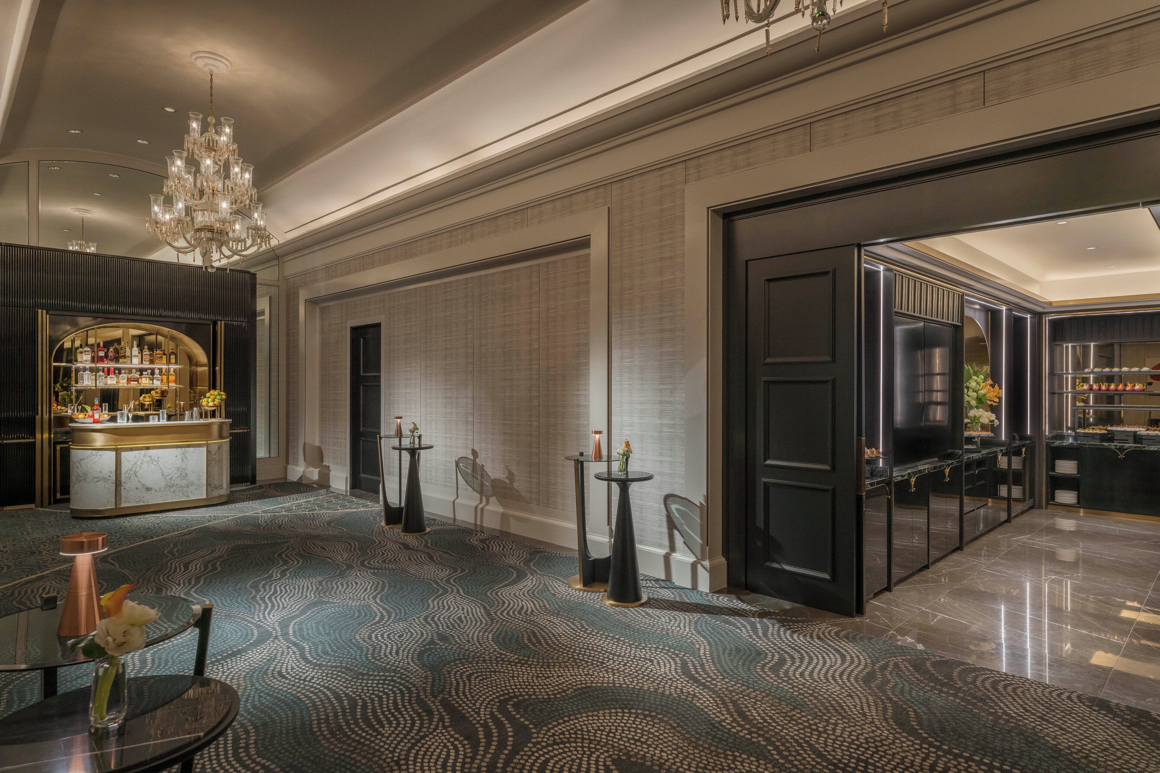 Un hall d’hôtel moderne avec un bar, un lustre et un tapis à motifs.