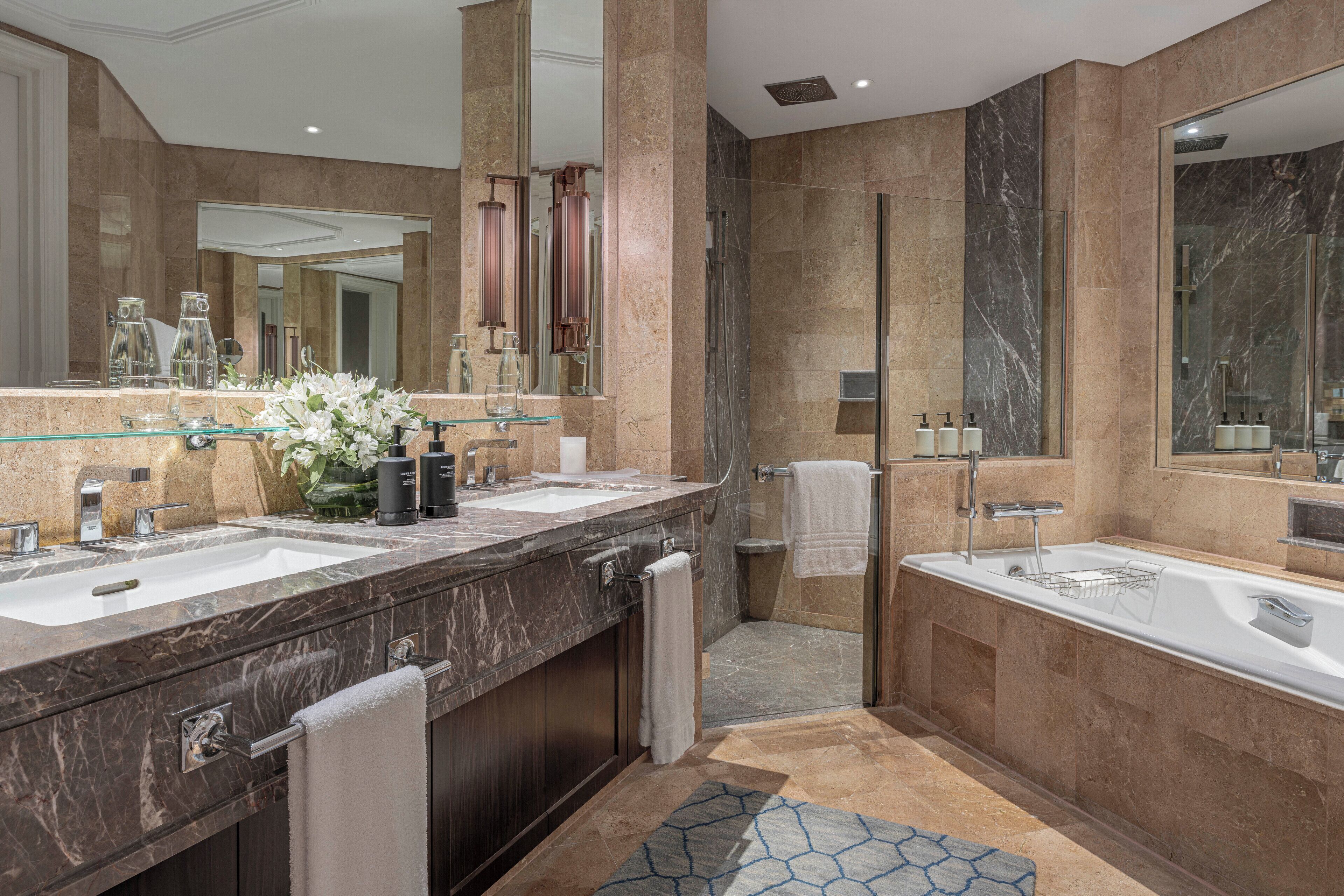 A modern bathroom with two sinks, a glass shower enclosure, marble walls, and a large mirror.