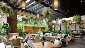 An indoor restaurant with wicker furniture, hanging plants, and a stone wall. - Four Seasons Hotel Singapore (Singapore)