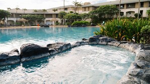 Une piscine bordée de rochers, entourée de palmiers et d’un bâtiment doté de balcons.