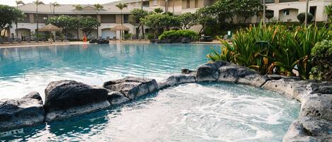 Una piscina con borde rocoso, rodeada de palmeras y un edificio con balcones.