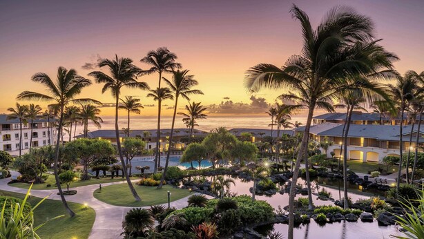 Un complexe hôtelier doté d’une piscine, de palmiers et offrant une vue sur l’océan au coucher du soleil.