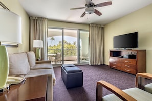 A hotel room with a sofa, a television, a desk, a lamp, a ceiling fan, and a view of palm trees through the balcony doors. - Hilton Vacation Club The Point At Poipu Kauai (Koloa)