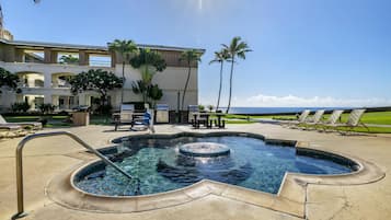 A pool area with a hot tub, lounge chairs, and a view of the ocean.