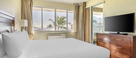 Une chambre d’hôtel avec un lit, une télévision, une commode et une fenêtre donnant sur des palmiers.