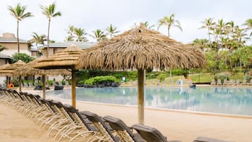 A poolside area with lounge chairs and thatched umbrellas, surrounded by palm trees and a clear sky.