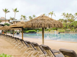 A poolside area with thatched umbrellas, lounge chairs, and a clear view of the pool.