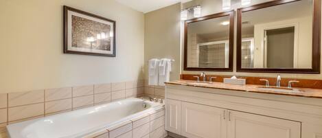A modern bathroom with a large bathtub, a double vanity with two sinks, and a large mirror above the vanity.