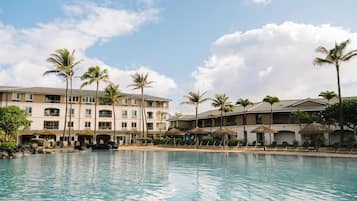 A hotel with a pool, palm trees, and a clear sky.
