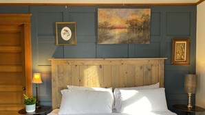 Ein ordentlich bezogenes Bett mit weißen Leinentüchern, einem hölzernen Kopfteil und einer blau gesteppten Bettdecke.