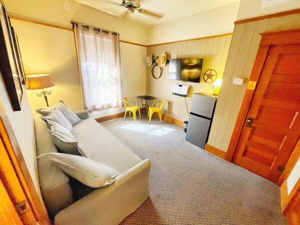 Una habitación de hotel compacta con una cama, una pequeña mesa con sillas, un refrigerador y un televisor en la pared.