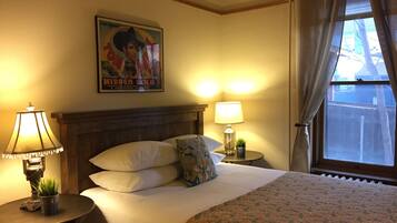 Quarto de hotel com uma cama grande, duas mesas de cabeceira com luminárias, um quadro na parede e uma janela com cortinas.