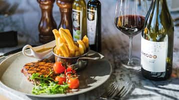 Une assiette avec un steak, des frites et des légumes, un verre de vin rouge et deux bouteilles de vin sur une table.